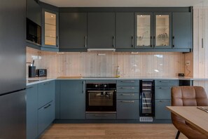 A modern kitchen with grey cabinets, a built-in oven, and a dining area with a wooden table and a brown chair.