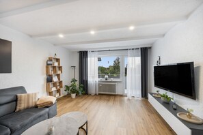 A modern living room with a grey sofa, a coffee table, a TV, and a bookshelf. - Apartment 'Weitblick' with Mountain View, Balcony, and Wi-Fi (Reute)