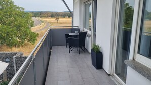 A balcony with a table and chairs, a potted plant, and a view of a road and fields. - Apartment 'Weitblick' with Mountain View, Balcony, and Wi-Fi (Reute)