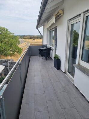 A balcony with a table and chairs, a potted plant, and a view of a road and fields. - Apartment 'Weitblick' with Mountain View, Balcony, and Wi-Fi (Reute)