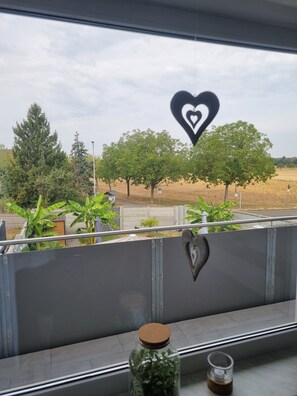 A balcony with a view of trees and a field, a heart-shaped decoration, and a glass jar with plants. - Apartment 'Weitblick' with Mountain View, Balcony, and Wi-Fi (Reute)