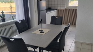 A dining area with a table and chairs, a kitchen in the background, and a view of the countryside through the window. - Apartment 'Weitblick' with Mountain View, Balcony, and Wi-Fi (Reute)