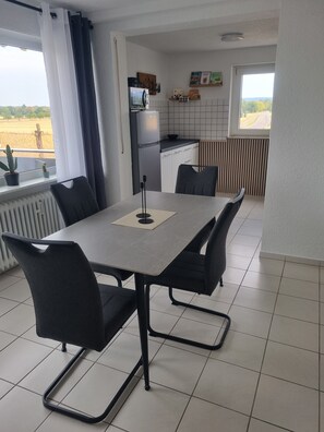 A dining area with a table and chairs, a kitchen in the background, and a view of the countryside through the window. - Apartment 'Weitblick' with Mountain View, Balcony, and Wi-Fi (Reute)