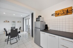 A modern kitchen with a refrigerator, microwave, and coffee maker. There is a dining area with chairs and a table. - Apartment 'Weitblick' with Mountain View, Balcony, and Wi-Fi (Reute)