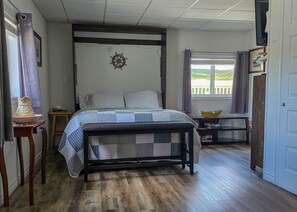 Een slaapkamer met een bed, een raam met gordijnen, een houten vloer en een aan de muur bevestigde decoratie van een scheepsschijf.