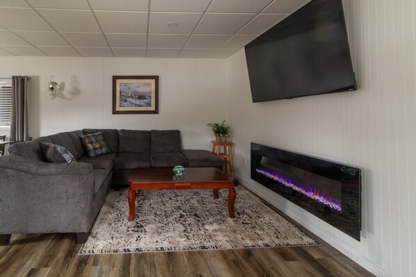 Een woonkamer met een modulaire bank, een salontafel, een open haard met glazen scherm en een flatscreen televisie aan de muur.