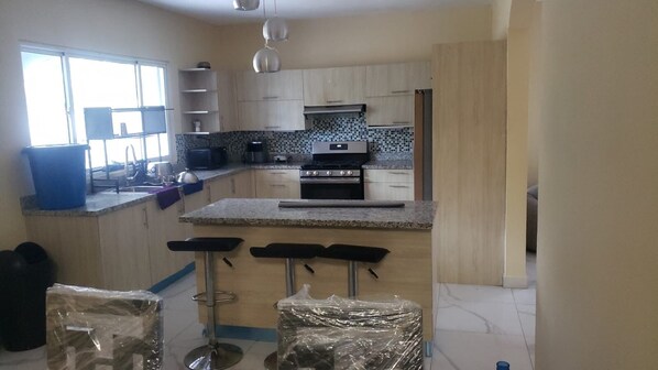 A kitchen with a central island, bar stools, and a stove. - Pa Sabana 1 Residence — ideal for families, groups, or business travelers. (Sabana Grande de Boyá)