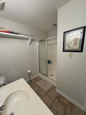 A bathroom with a white sink, a glass shower enclosure, a towel rack with folded towels, and a framed artwork on the wall.