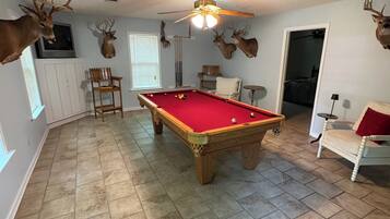 A room with a pool table, a ceiling fan, and mounted deer heads on the walls.