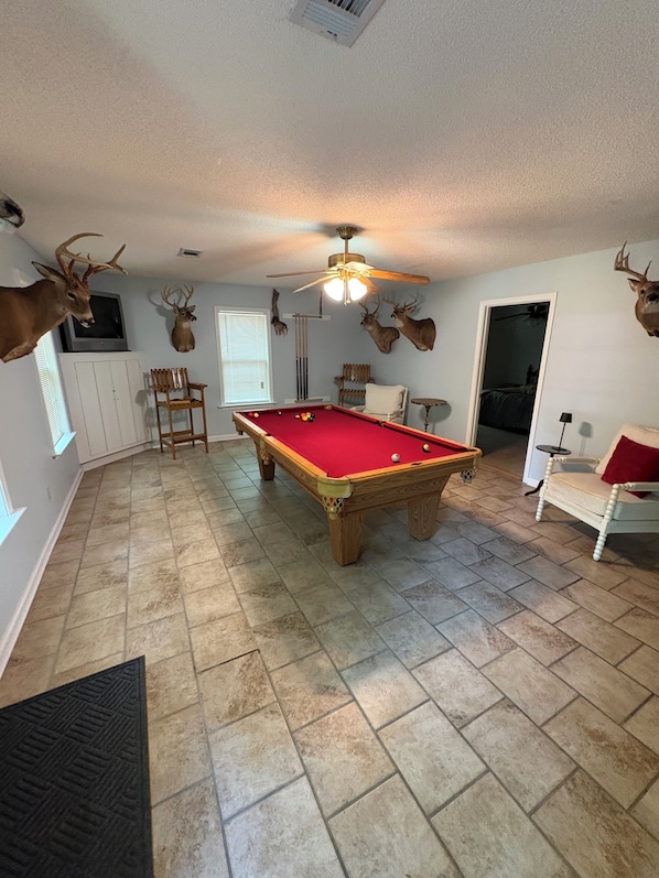 A room with a pool table, a ceiling fan, and mounted deer heads on the walls.