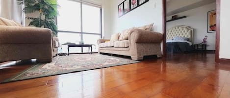 A spacious living room with a large window, a sofa, a coffee table, and a rug.