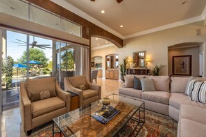 A spacious living room with a glass coffee table, beige sofas, and a view of the outdoors. - Fairway Peaks at PGA West | Mountain & Golf Views (La Quinta)