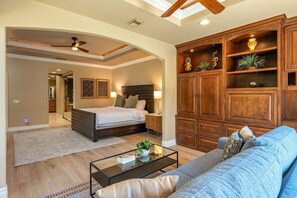 A spacious living room with a large bed, a wooden cabinet, and a glass coffee table. - Fairway Peaks at PGA West | Mountain & Golf Views (La Quinta)