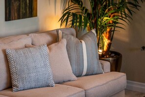 A beige sofa with patterned pillows and a potted plant in the background. - Fairway Peaks at PGA West | Mountain & Golf Views (La Quinta)