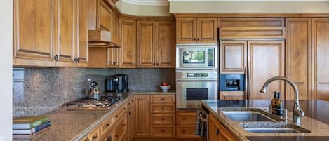 Une cuisine dotée de meubles en bois, de plans de travail en granit, d’appareils électroménagers en acier inoxydable et d’un four encastré.