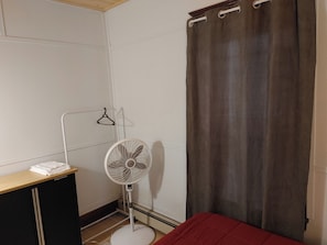 A room with a bed, a white standing fan, a heater, a wardrobe, and a curtain.
