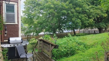 A backyard with a barbecue grill, a wooden deck, and a wooden fence.
