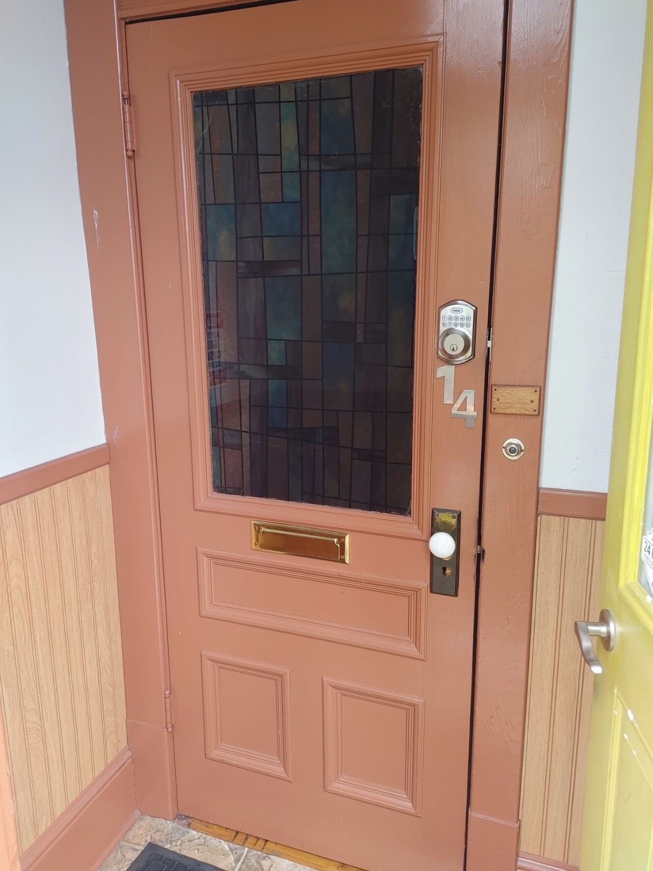 A brown door with a glass panel, a keypad lock, and a mailbox.