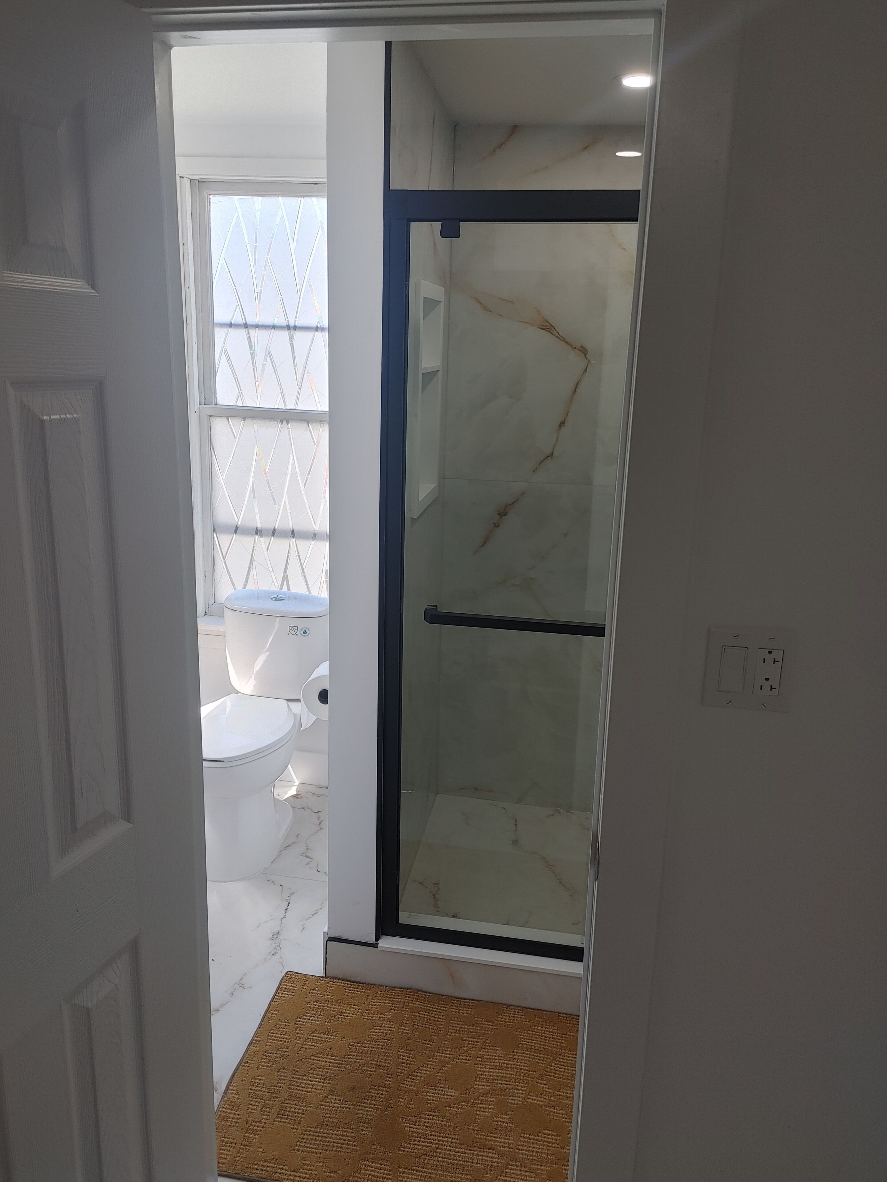 A bathroom with a toilet, a shower with glass doors, and a white marble floor.