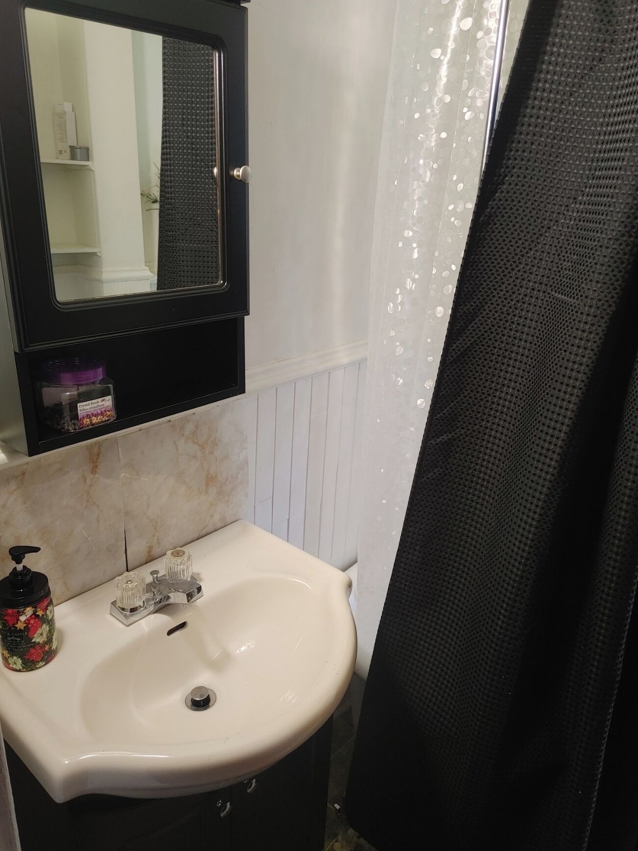 Ein Badezimmer mit einem weißen Waschbecken, einem Spiegel darüber und einer Duschvorhang.