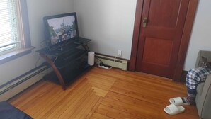 A room with a wooden floor, a television on a stand, a door, and a window with blinds. - Economy Sweet Room No. 5, Double bed, non ac (Saint John)