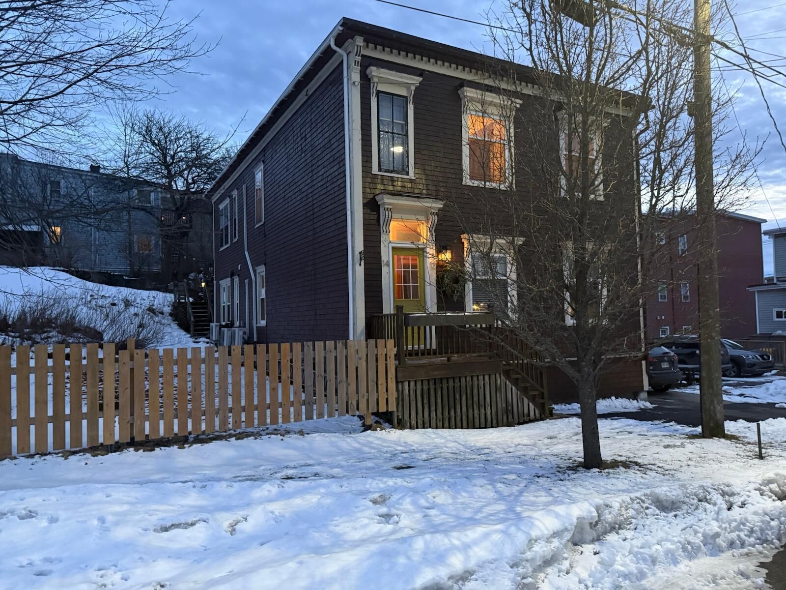 Une maison à deux étages avec une véranda en bois et une clôture faite de piquets.