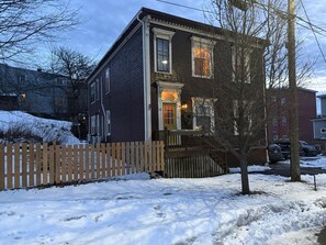 Une maison à deux étages avec une véranda en bois et une clôture faite de piquets.
