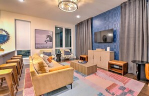 Ein modernes Wohnzimmer mit einer Couch, einem Couchtisch und einem Fernseher. Holzschemeln, ein Schrank und ein gemustertes Teppich sind ebenfalls vorhanden.