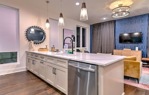 A modern kitchen with a central island, stainless steel appliances, pendant lighting, and a large window. - Lux Nash Stay: Private Hot Tub, Rooftop & 12 Beds! (Nashville)