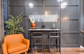Ein modernes Interieur mit dunkler Wand, einer Neonreklame, einer Pflanze, einem orangefarbenen Sessel und einer Bar.