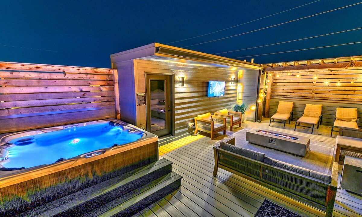 A hot tub and outdoor seating area with a television on a wall.