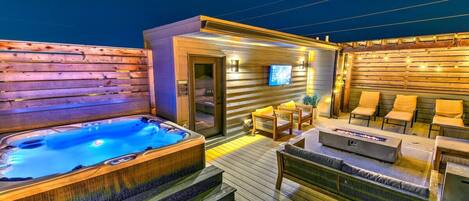 A hot tub and outdoor seating area with a television on a wall.