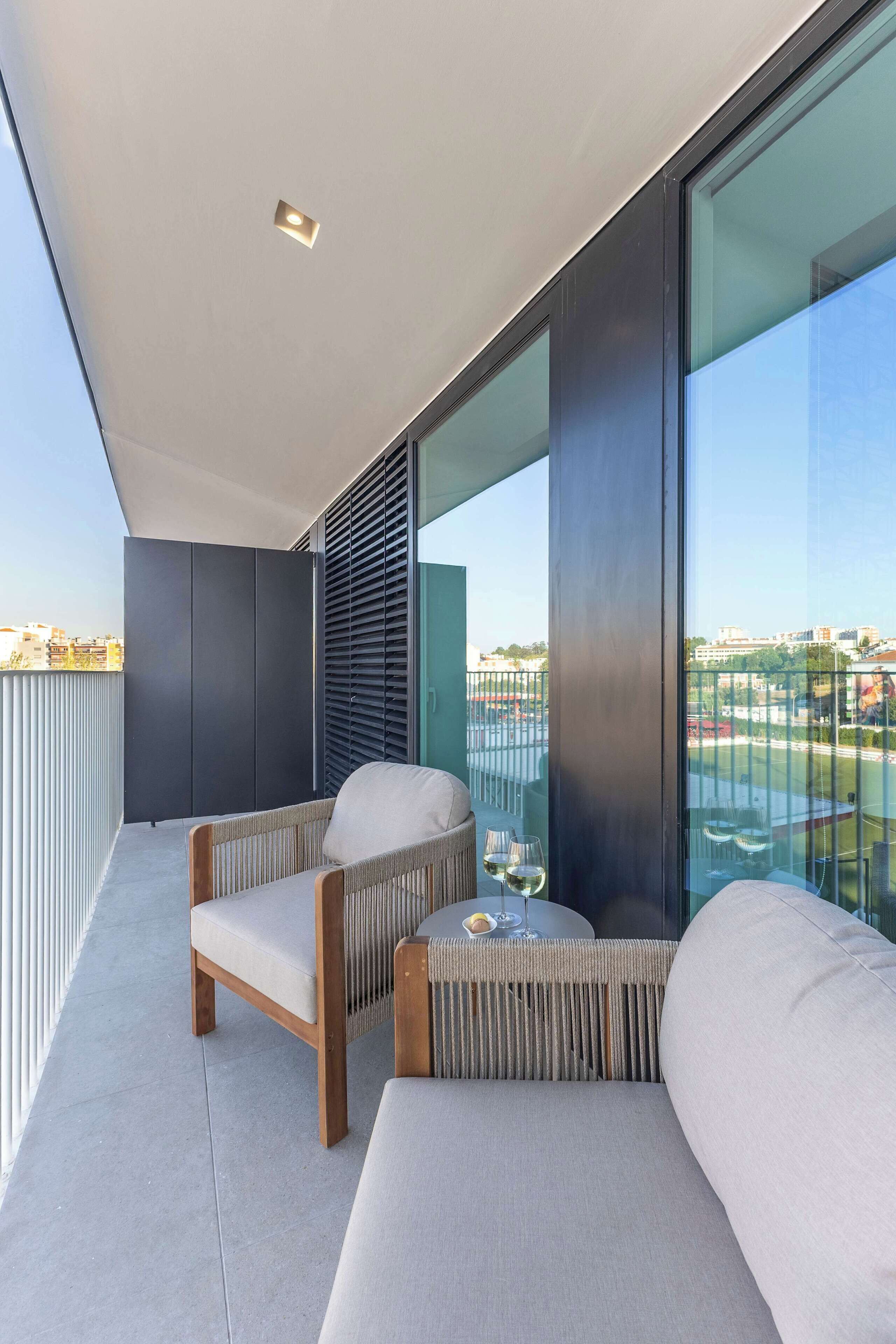 Un balcon avec deux canapés et une table, une rambarde en verre et une vue sur la ville.