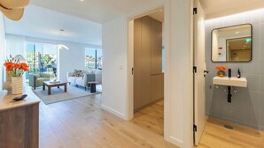 A modern hotel room with a wooden floor, a sitting area with a sofa and coffee table, a bathroom with a sink and mirror, and a view of the city through large windows. - Sky Pool Luxury by Portugal Active (Barreiro)