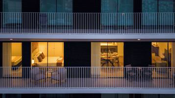 A modern building with a balcony, large windows, and a dining area visible through the glass.