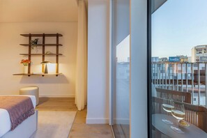 Ein modernes Hotelzimmer mit Balkon, einem Nachttisch mit Lampe und Blick auf die Stadt.