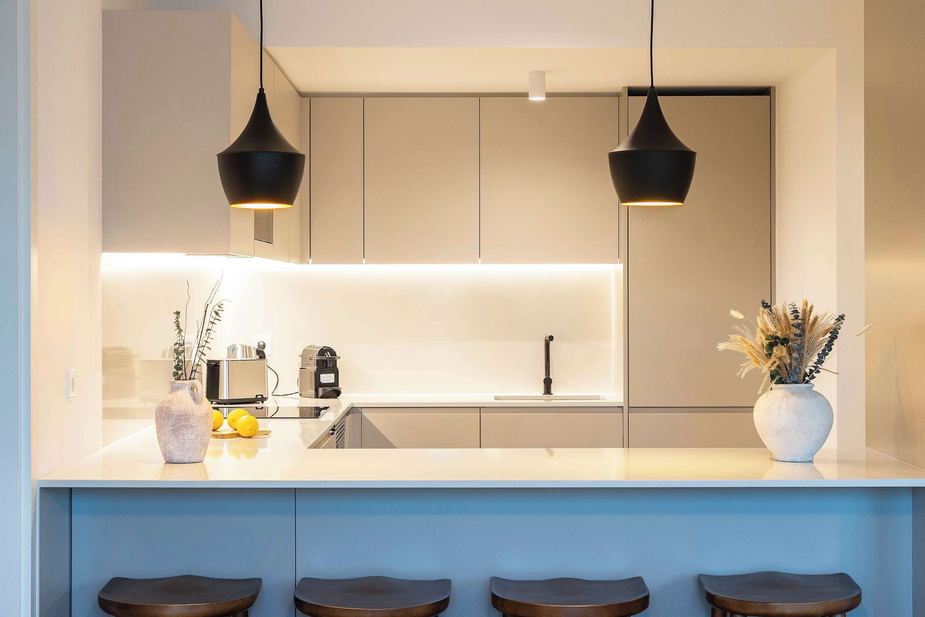 Una cucina moderna con isola centrale, sgabelli da bar, illuminazione a sospensione e lavello.