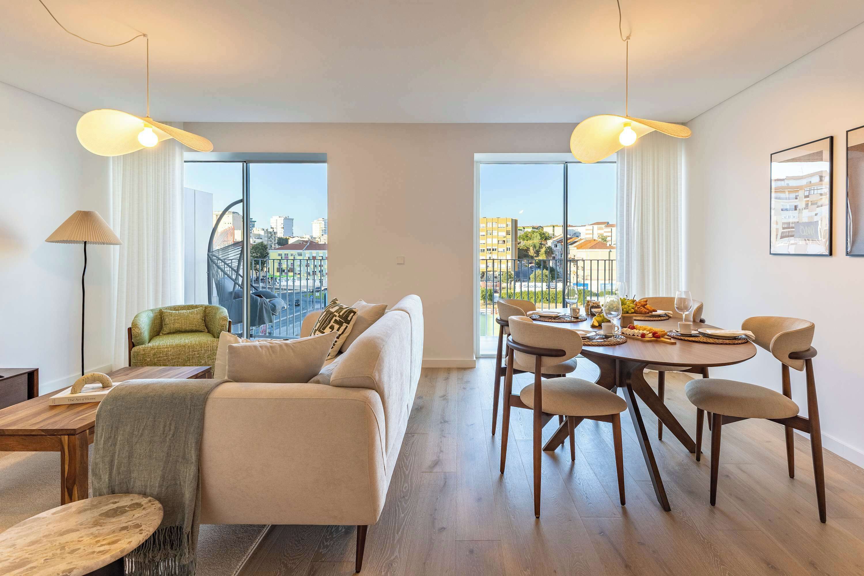 Ein modernes Wohnzimmer mit einer Couch, einem Esstisch mit Stühlen und Blick auf die Stadt durch große Fenster.