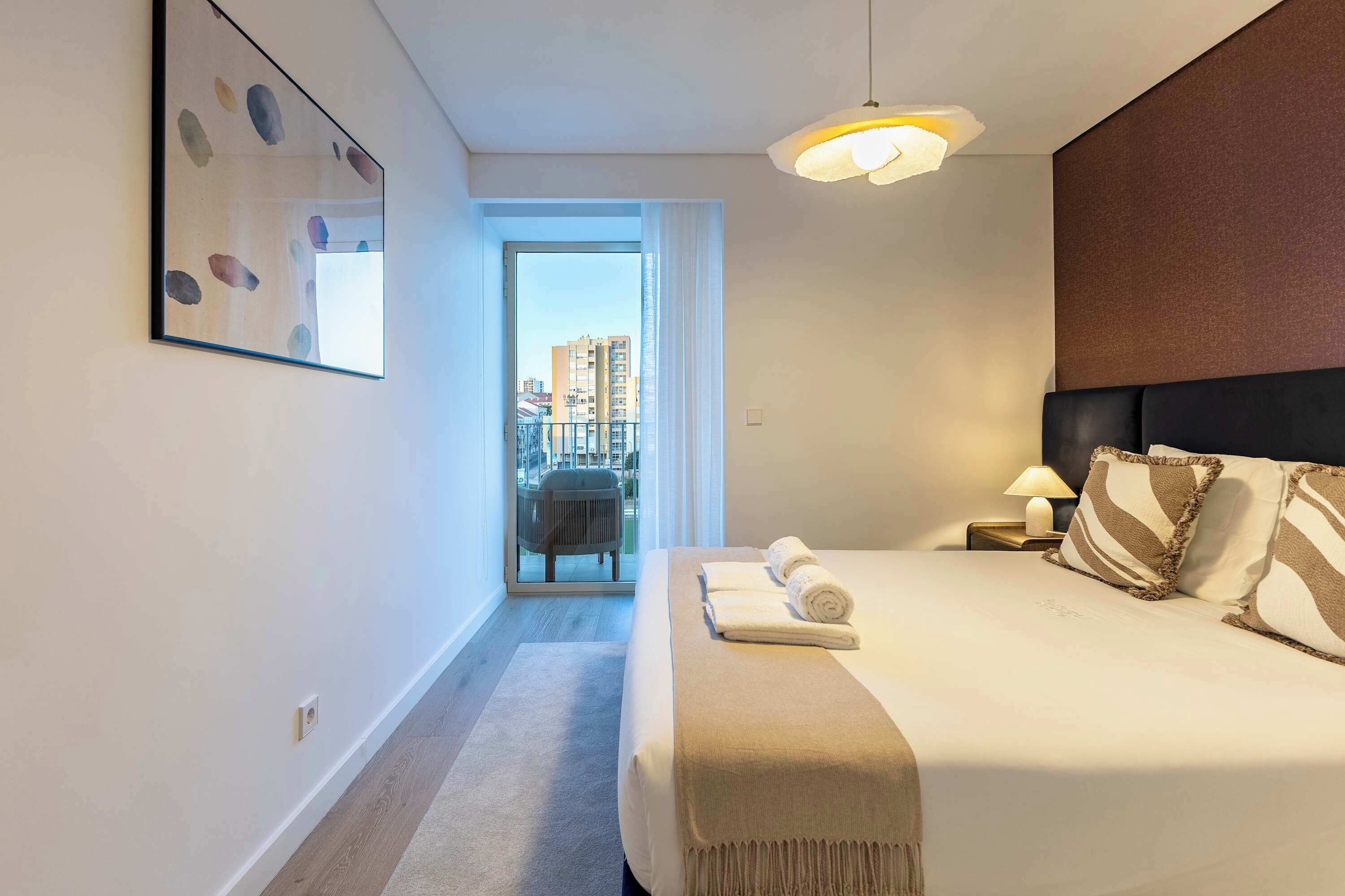 Une chambre d’hôtel avec un lit, une table de chevet, une lampe, une chaise et une vue sur la ville par la fenêtre.
