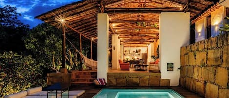 A pool area with a thatched roof structure, stone walls, and a view of the interior.