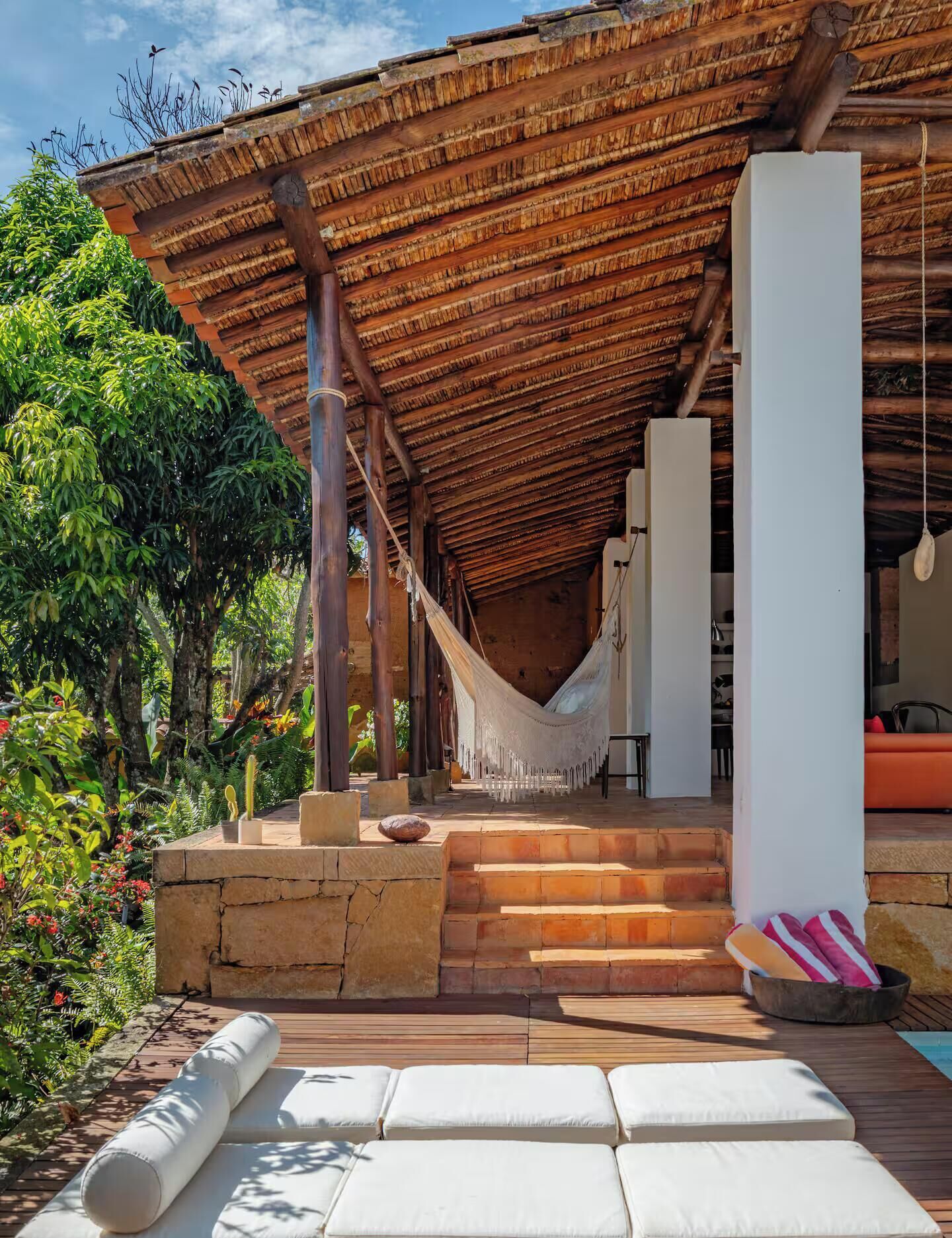 A covered outdoor area with a hammock, steps leading to a seating area, and a pool.