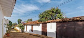 Una calle estrecha con edificios blancos, un árbol con flores anaranjadas y una puerta de garaje marrón.