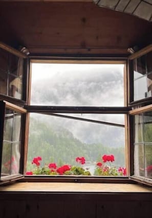 A room with a large window overlooking a mountainous landscape with greenery and a body of water.