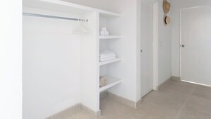 A hallway with a white closet, a door with a hat on the wall, and a tiled floor.