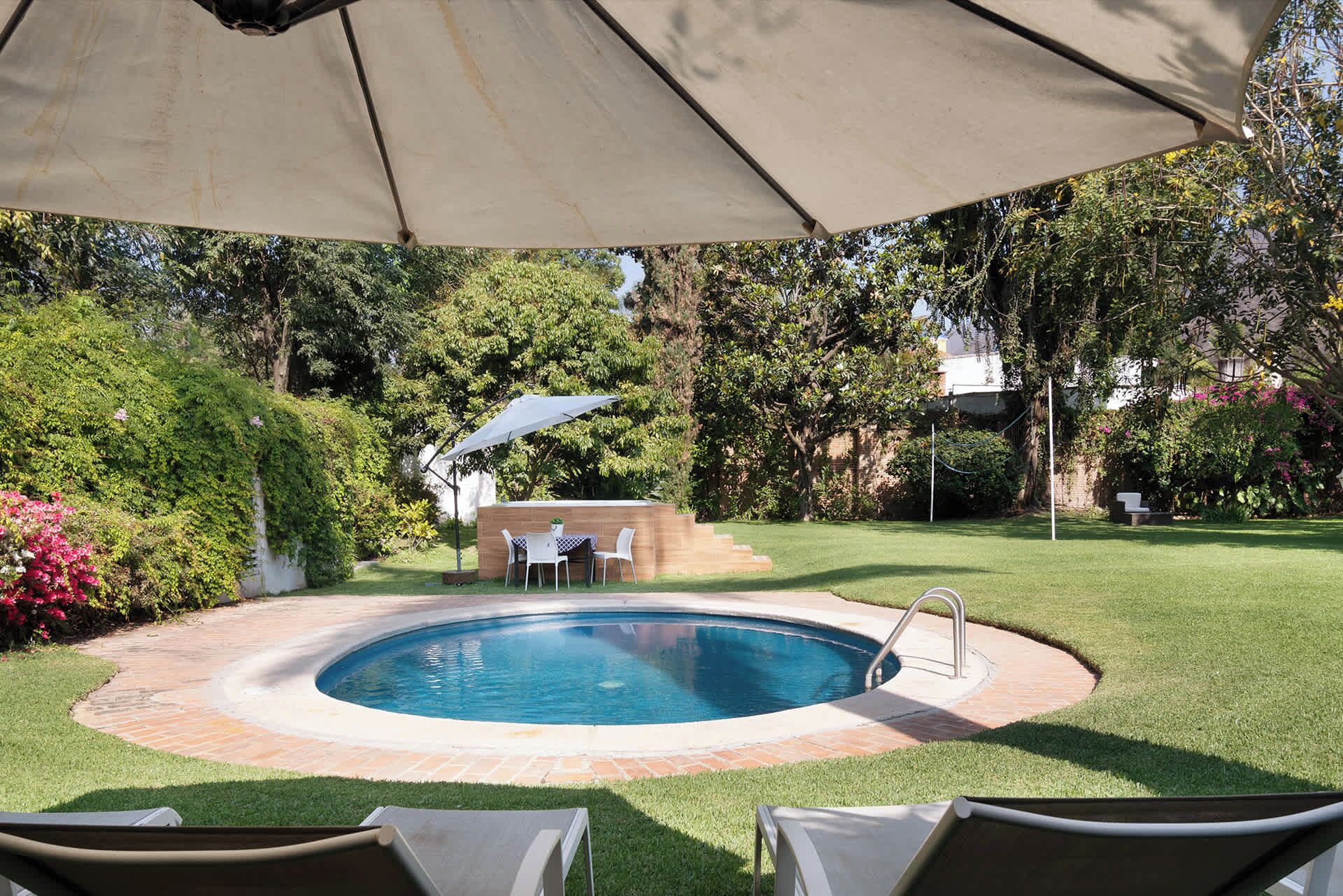 Une piscine extérieure avec un espace patio, entourée de pelouse et d’arbres.