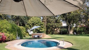 An outdoor swimming pool with a patio area, surrounded by grass and trees.