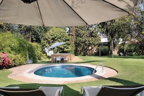 An outdoor swimming pool with a patio area, surrounded by grass and trees.