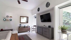 A modern living room with a flat-screen TV, a ceiling fan, and a large window.