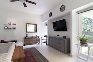 A modern living room with a flat-screen TV, a ceiling fan, and a large window.