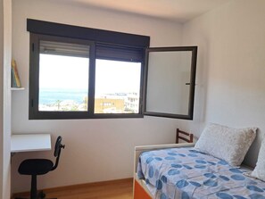 Ein Schlafzimmer mit einem Bett, einem Schreibtisch und einem Fenster mit Blick auf Gebäude und das Meer.